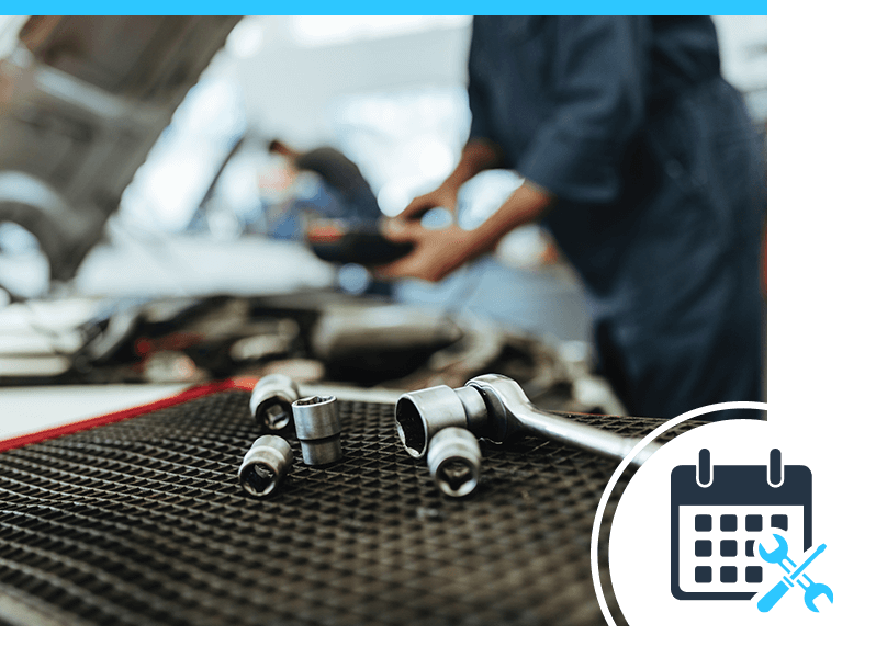 A set of tools on a work bench with a technician working on a car in the background
